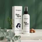 A bottle and box of Hoegoa Heat Agent heat protectant styler, shown on a light stone surface with eucalyptus leaves and argan nuts against a dark green background.