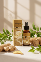 Biotin & Ginger Hair Serum Spray lifestyle photo — amber bottle and gold box on white linen with ginger root